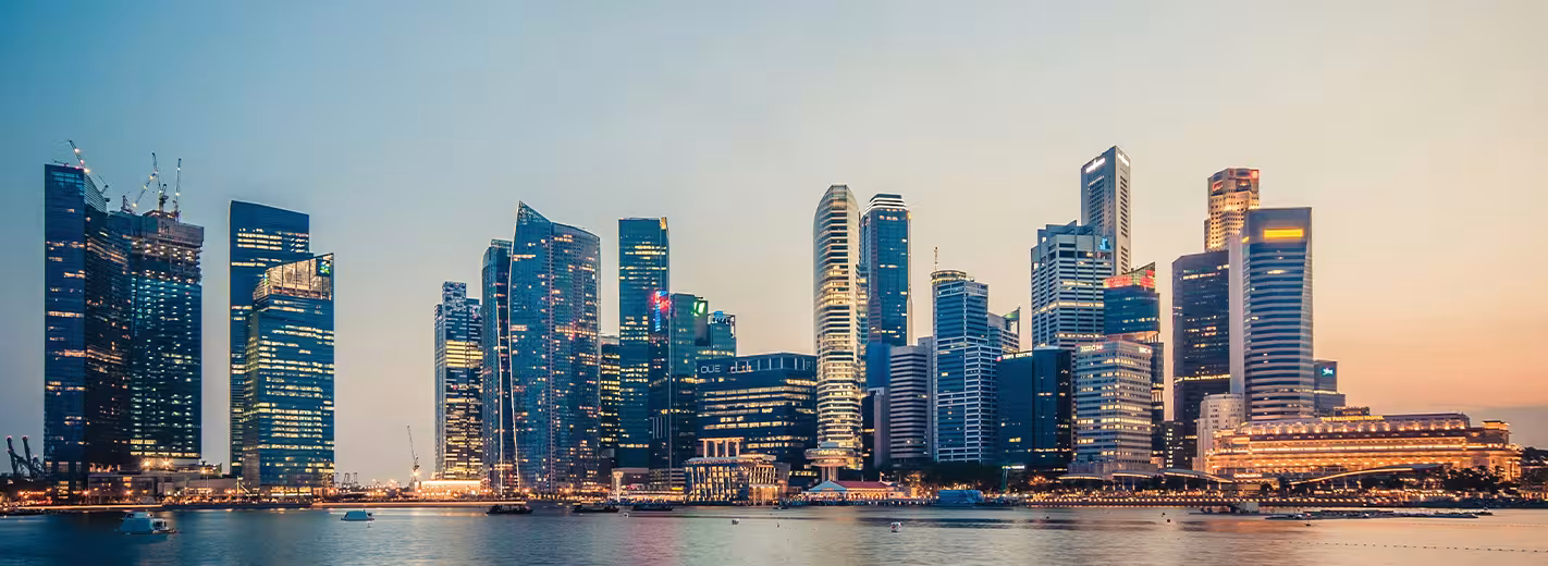 El horizonte de una ciudad al anochecer, que muestra los contornos oscuros de los edificios contra un cielo degradado de tonos naranjas, rosas y azules.