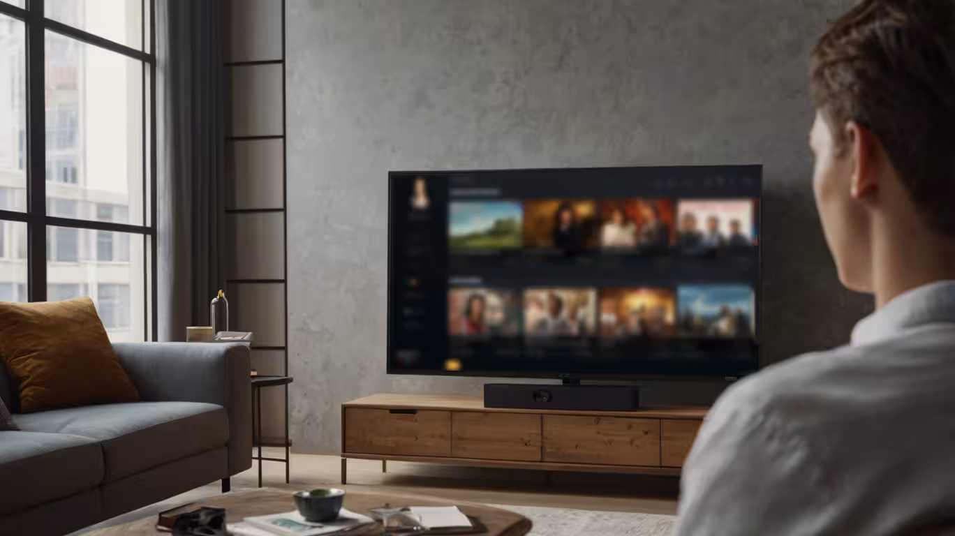 A man sits in a living room, focused on a television screen in front of him.
