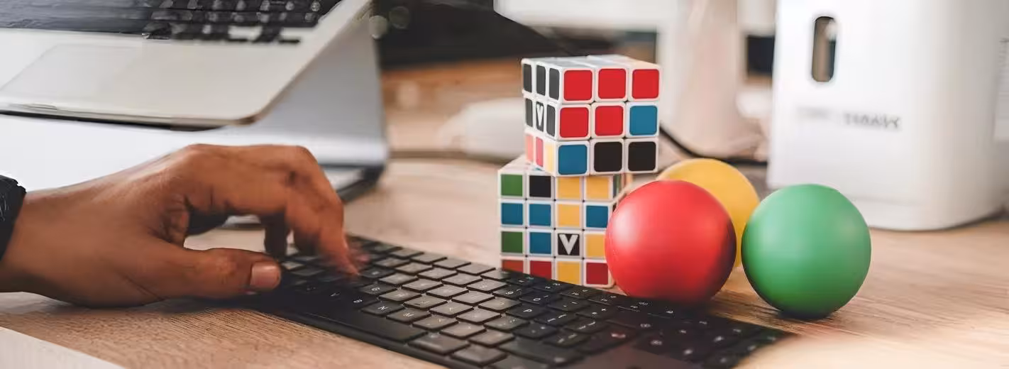 Una persona está escribiendo en el teclado de una computadora con un cubo de Rubik y una manzana cerca.