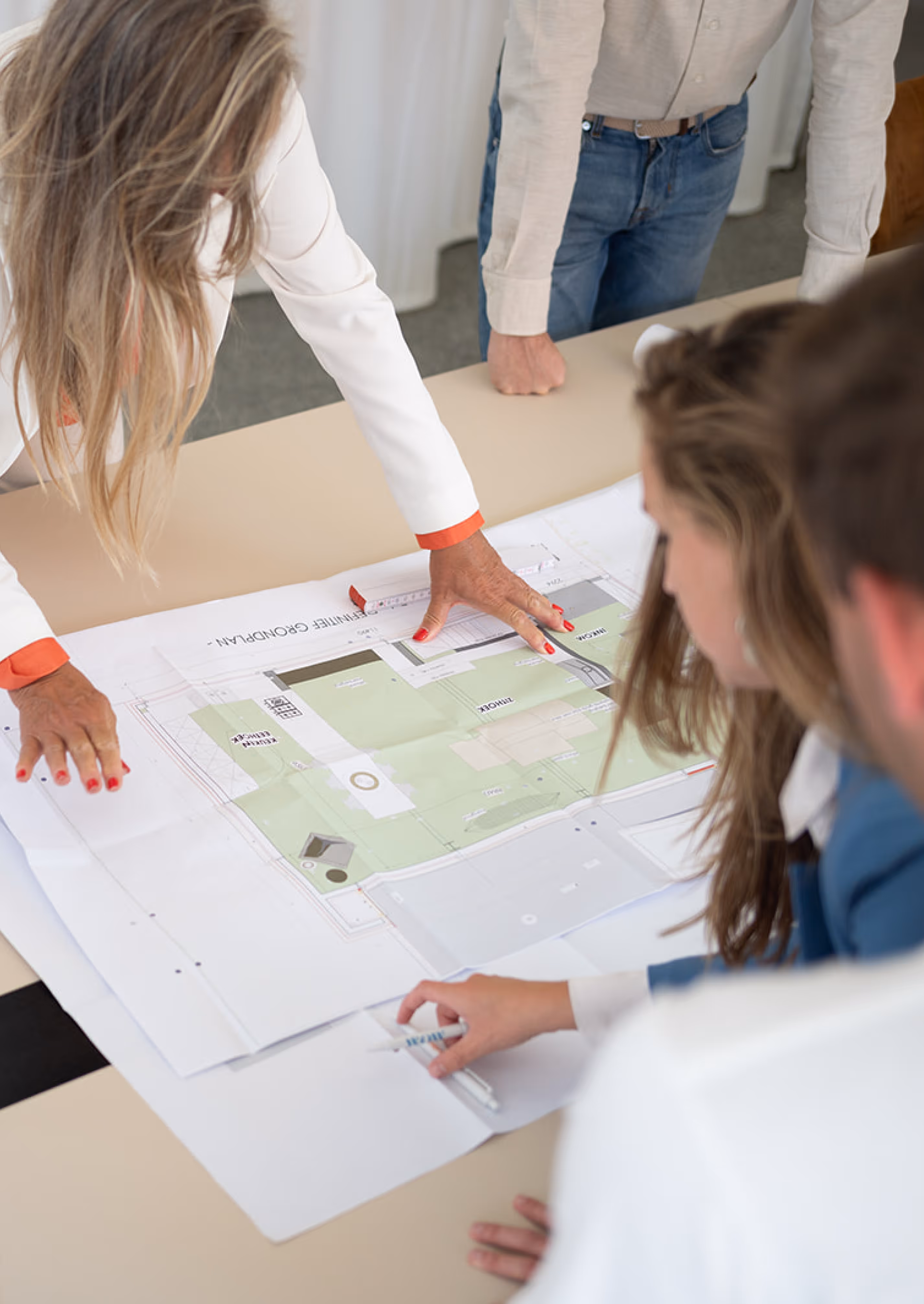 Mensen die over een tafel gebogen zijn en een bouwplan bespreken.