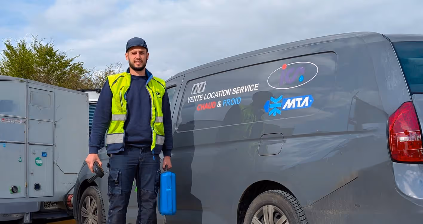 Technicien en veste jaune réfléchissante tenant une valise bleue debout à côté d'un fourgon gris avec les mots « Vente Location Service Chaud & Froid » écrits sur le côté.
