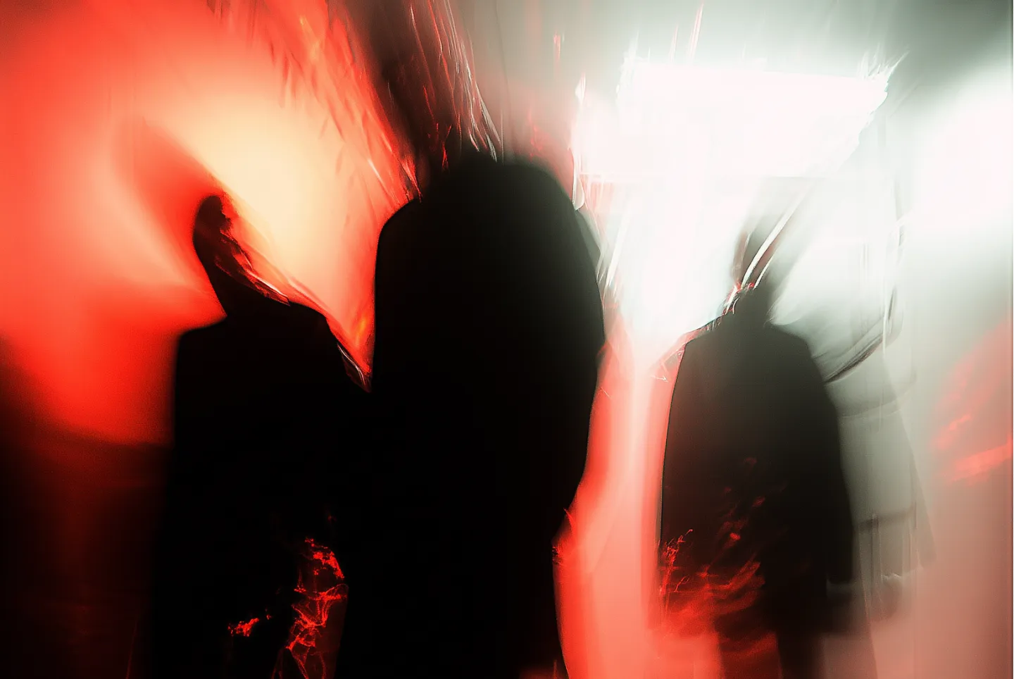 Blurred silhouettes of three people against a red and white illuminated background creating a mysterious and abstract effect.