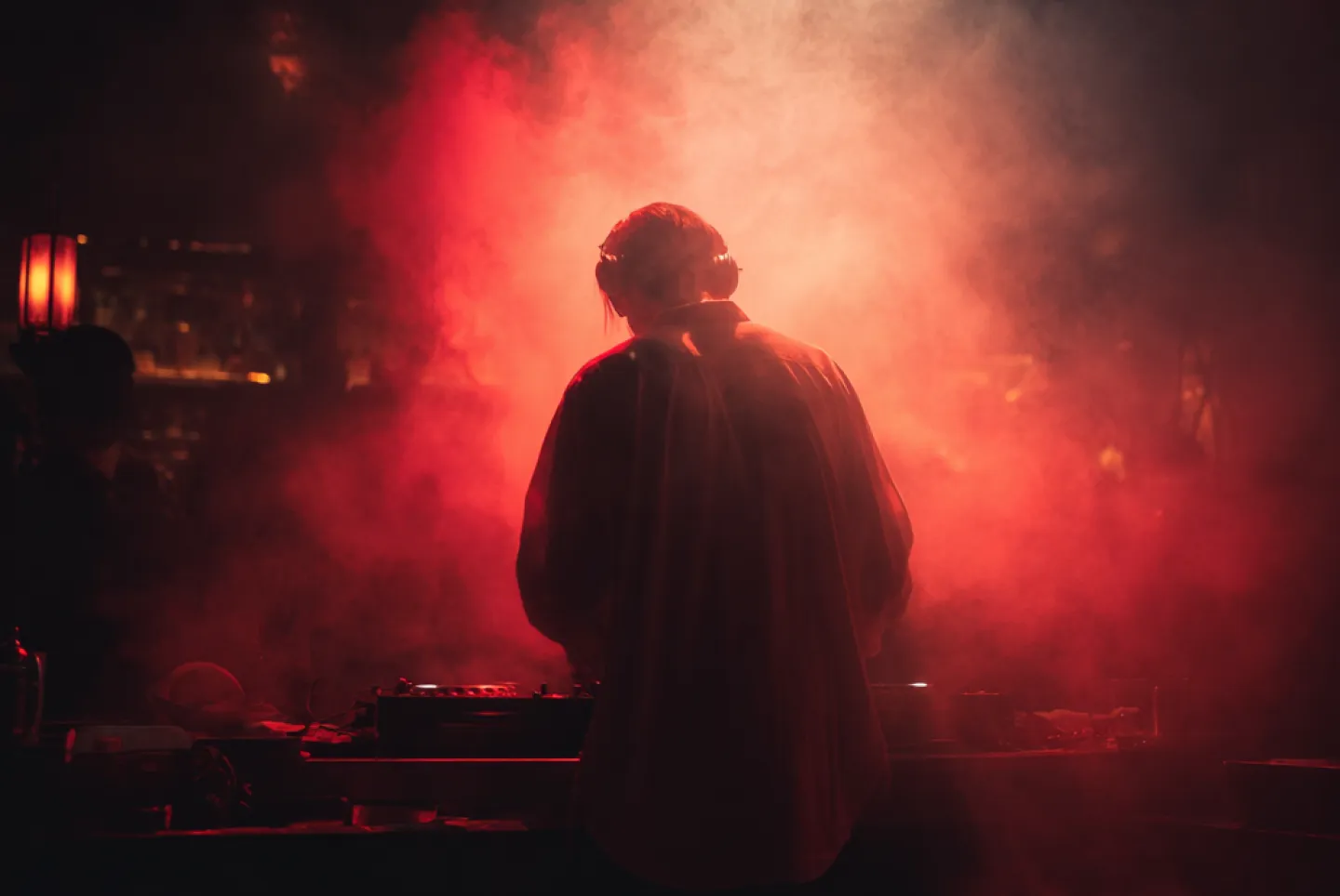 DJ wearing headphones performing amid red stage smoke and lighting.