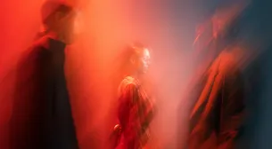 Blurred silhouettes of three people standing in red and orange light.