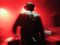 DJ wearing headphones performing on stage with vibrant red lighting and blurred crowd in the background.