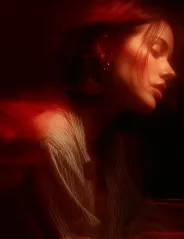 Softly lit profile of a woman with closed eyes and red highlights in her hair against a dark background.