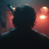 Silhouette of a person with curly hair in a dimly lit room with orange and blue lighting.