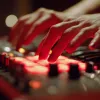 Hands adjusting knobs and controls on an electronic music mixer with red lighting.