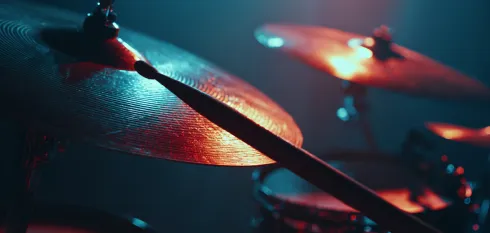 Close-up of a drumstick striking a cymbal on a drum set with warm lighting.