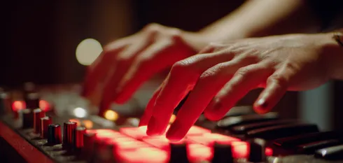 Hands playing on a music production controller with illuminated red pads and keyboard keys.