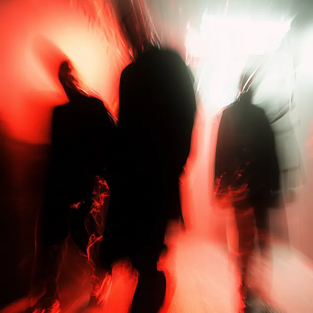 Blurry silhouettes of three people standing in a dimly lit hallway with red and white lighting.