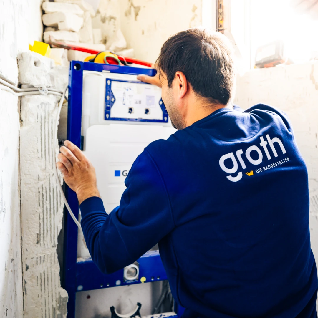 Handwerker montiert ein Gehäuse für eine Sanitärinstallation in einem unfertigen Raum.