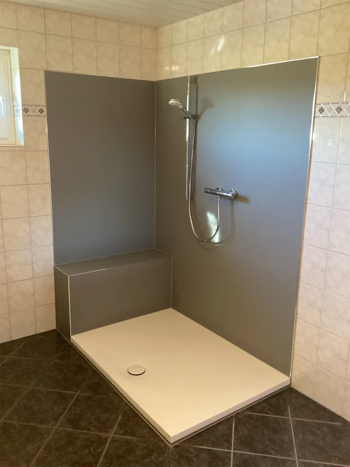 Barrierefreie Dusche mit beigem Duschboden, grauen Rückwänden, Handbrause und Sitzbank.