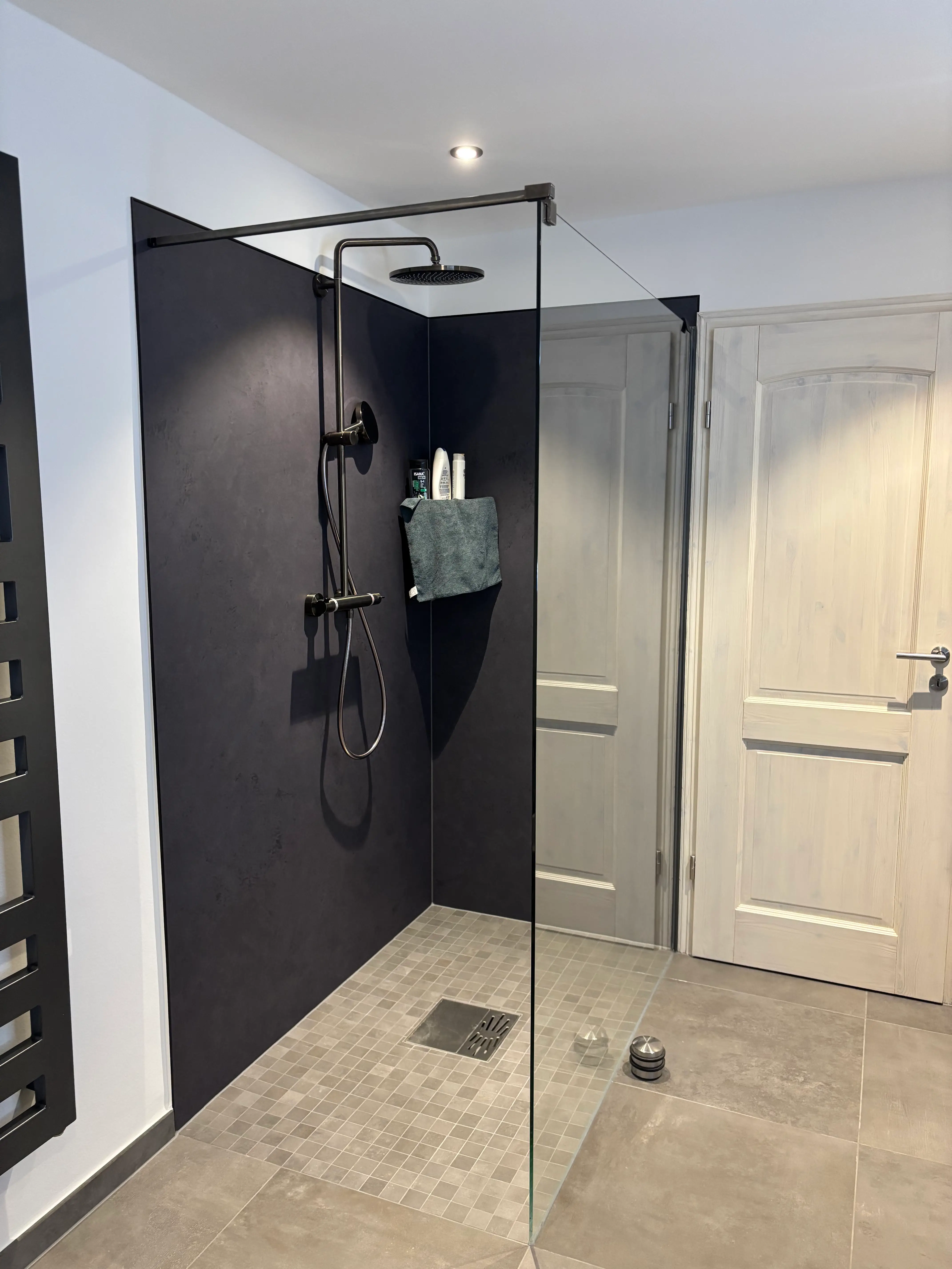 Moderne barrierefreie Dusche mit schwarzer Armatur, grauen Fliesen und Glastrennwand in einem Badezimmer.