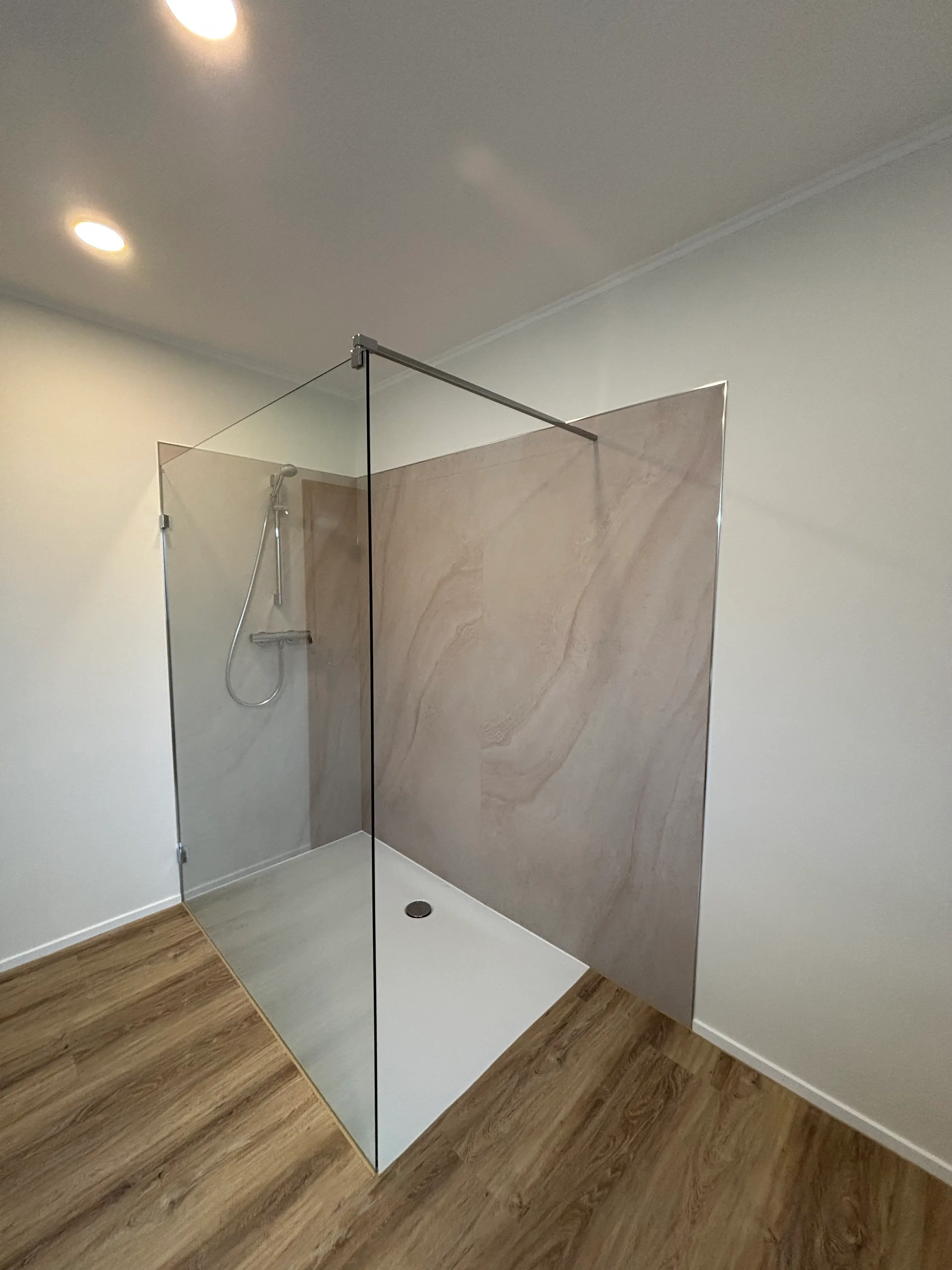 Minimalistische begehbare Dusche mit Glaswand, weißen Wänden und Holzoptikbodenbelag.