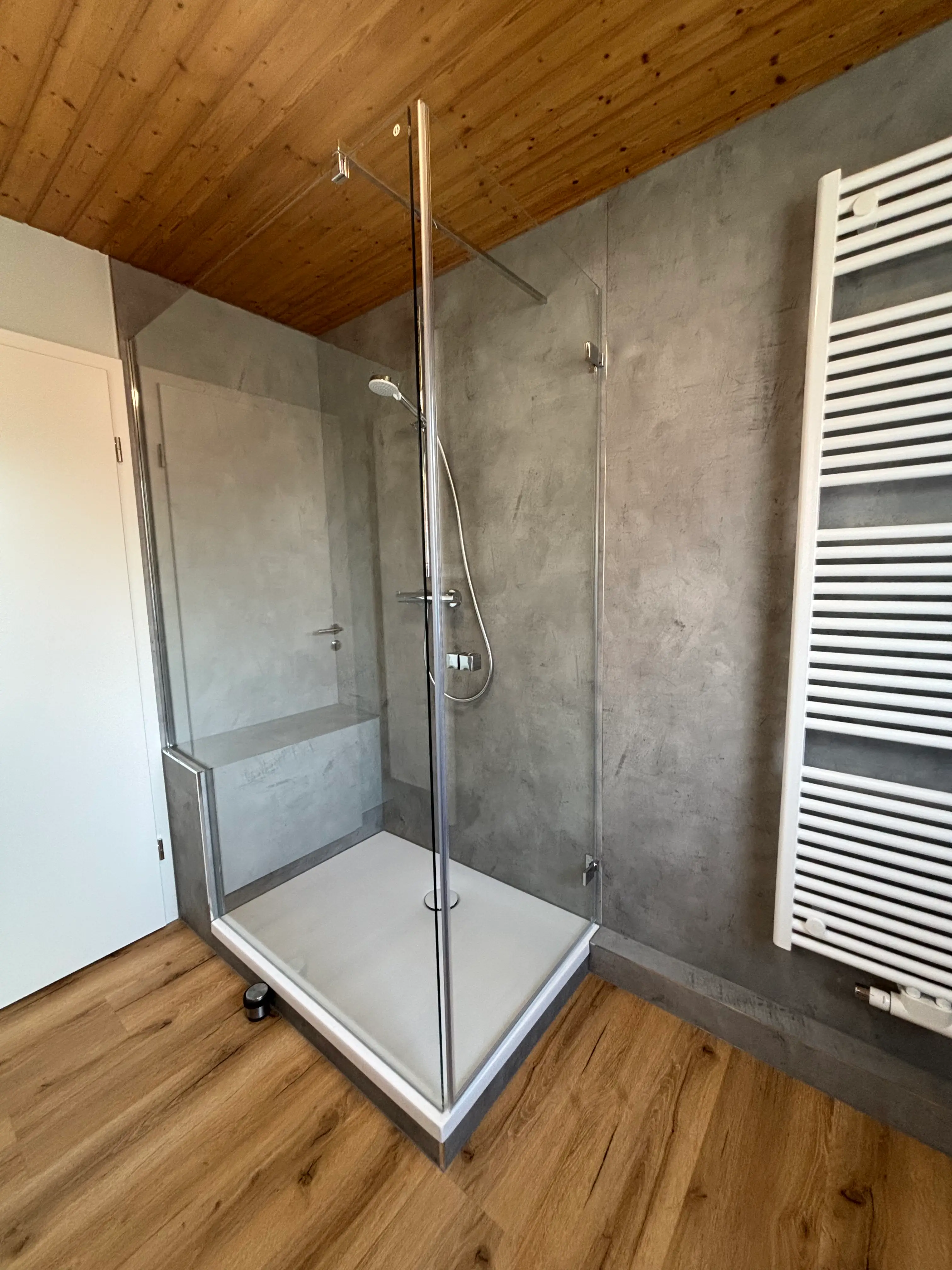 Modern barrierefreie Dusche mit transparenten Glaswänden, integriertem Sitz und Holzboden im Badezimmer.