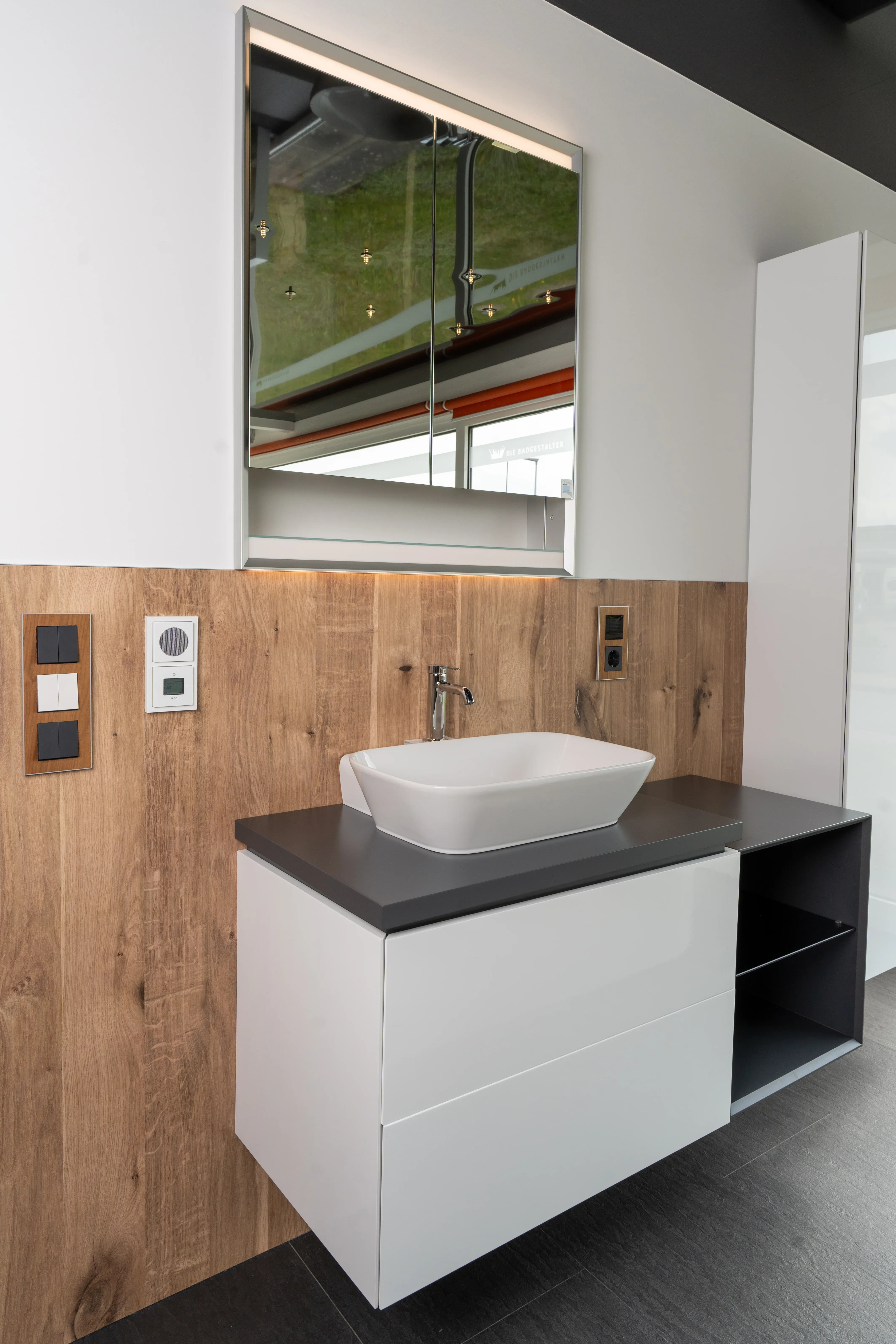 Modernes Badezimmer mit weißem wandhängendem Waschbecken auf schwarzer Arbeitsplatte und Holzvertäfelung an der Wand.