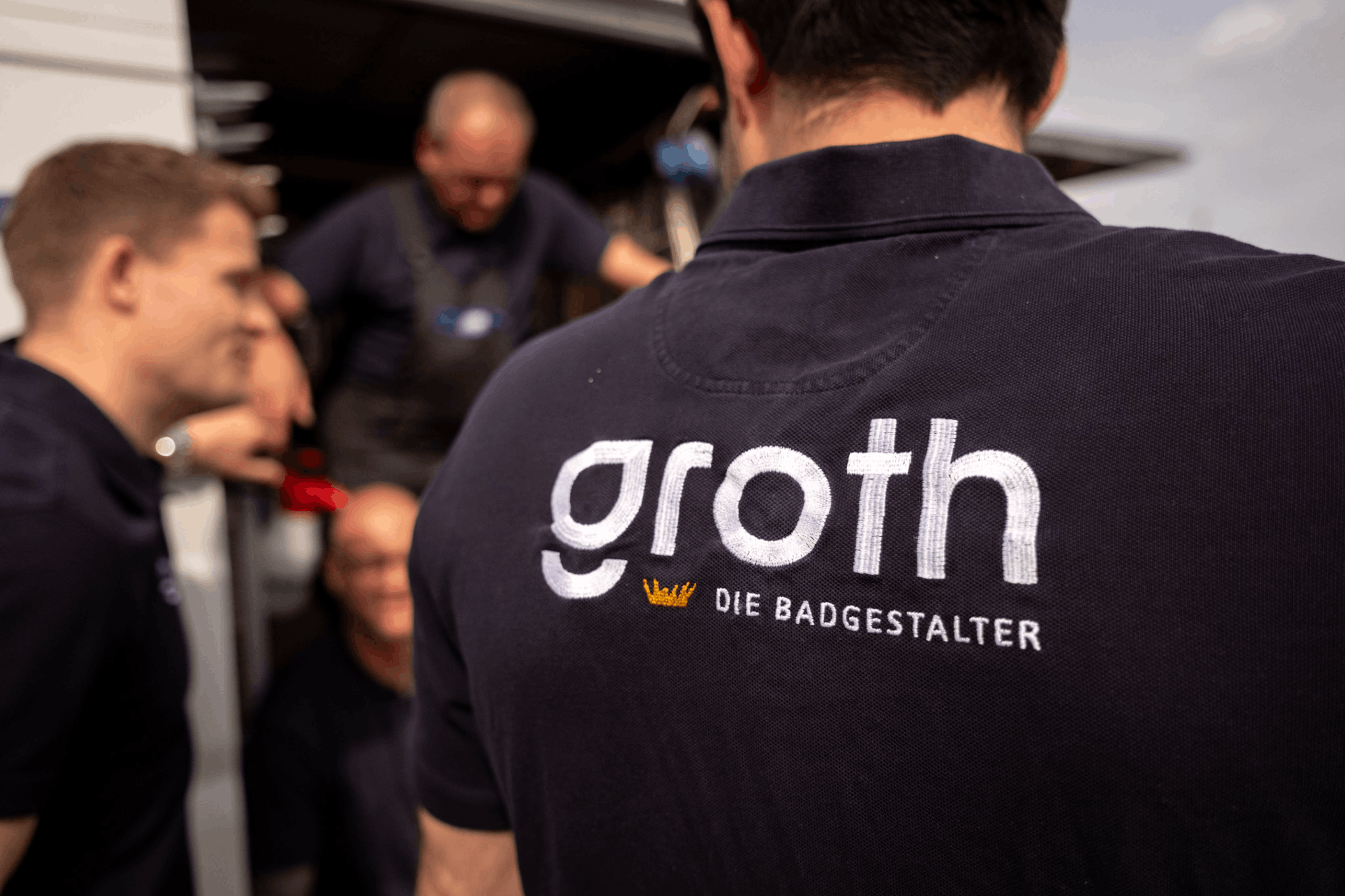 Zwei Männer vergleichen eine Holzmusterprobe und ein Blatt mit Text in einem hellen Raum.