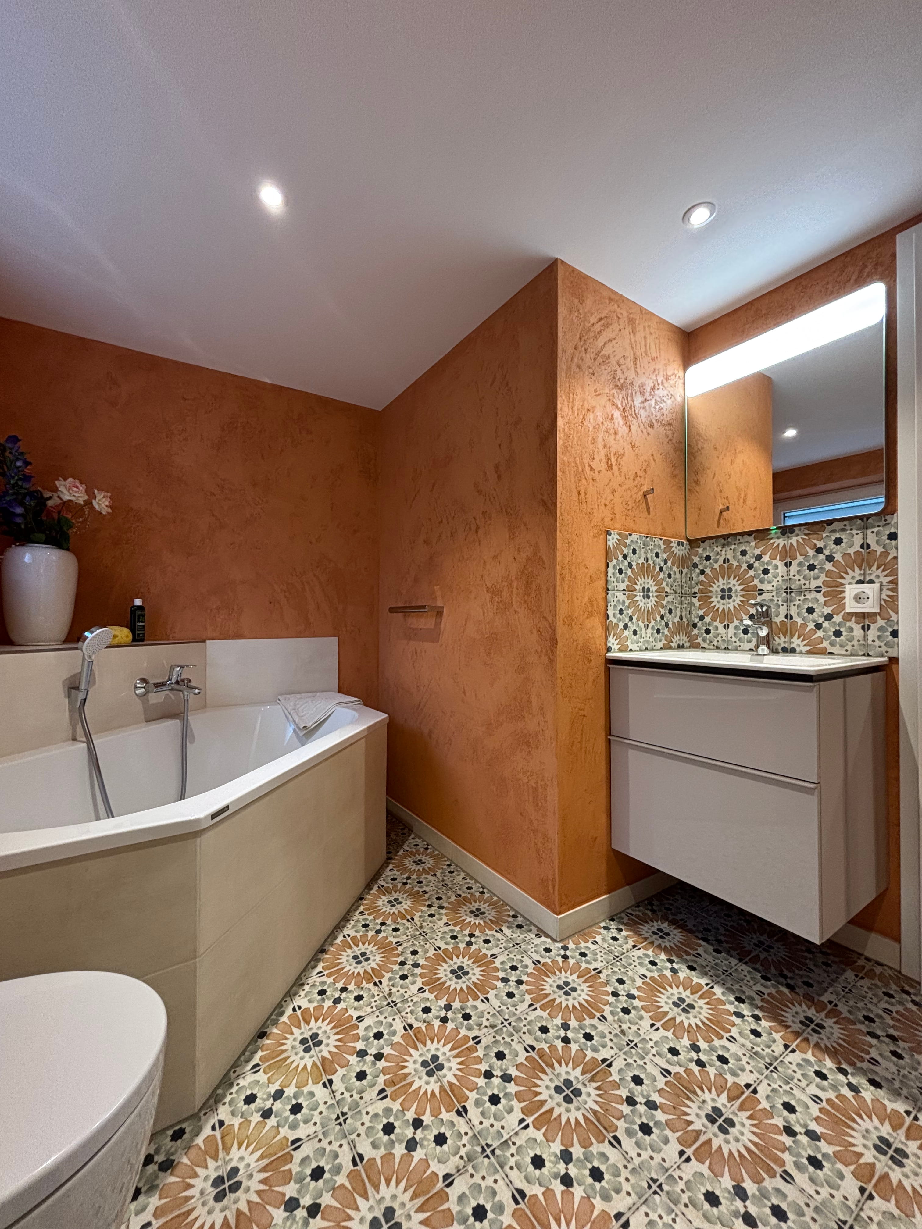 Barrierefreie Dusche mit beigem Duschboden, grauen Rückwänden, Handbrause und Sitzbank.