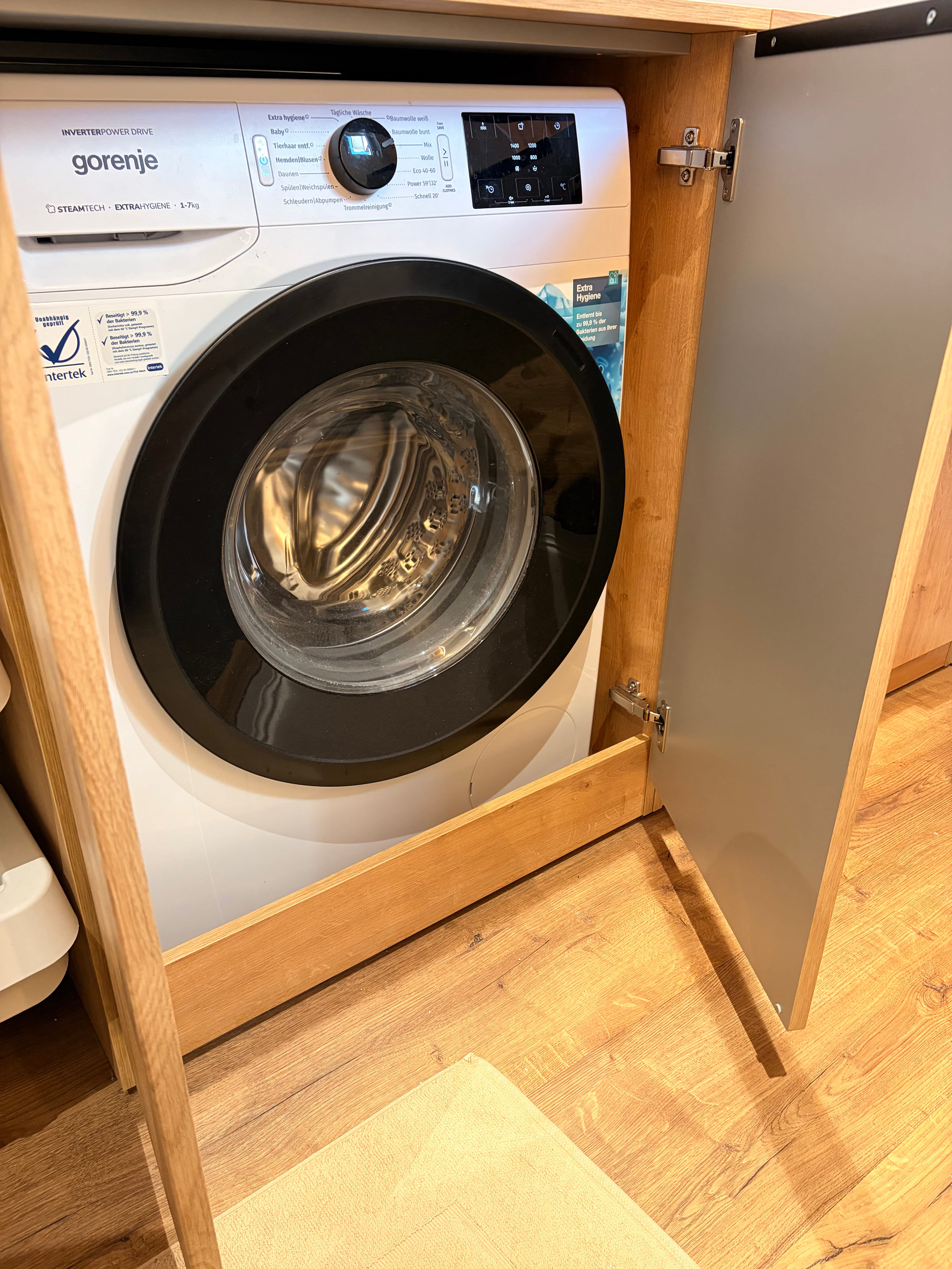 Barrierefreie Dusche mit beigem Duschboden, grauen Rückwänden, Handbrause und Sitzbank.