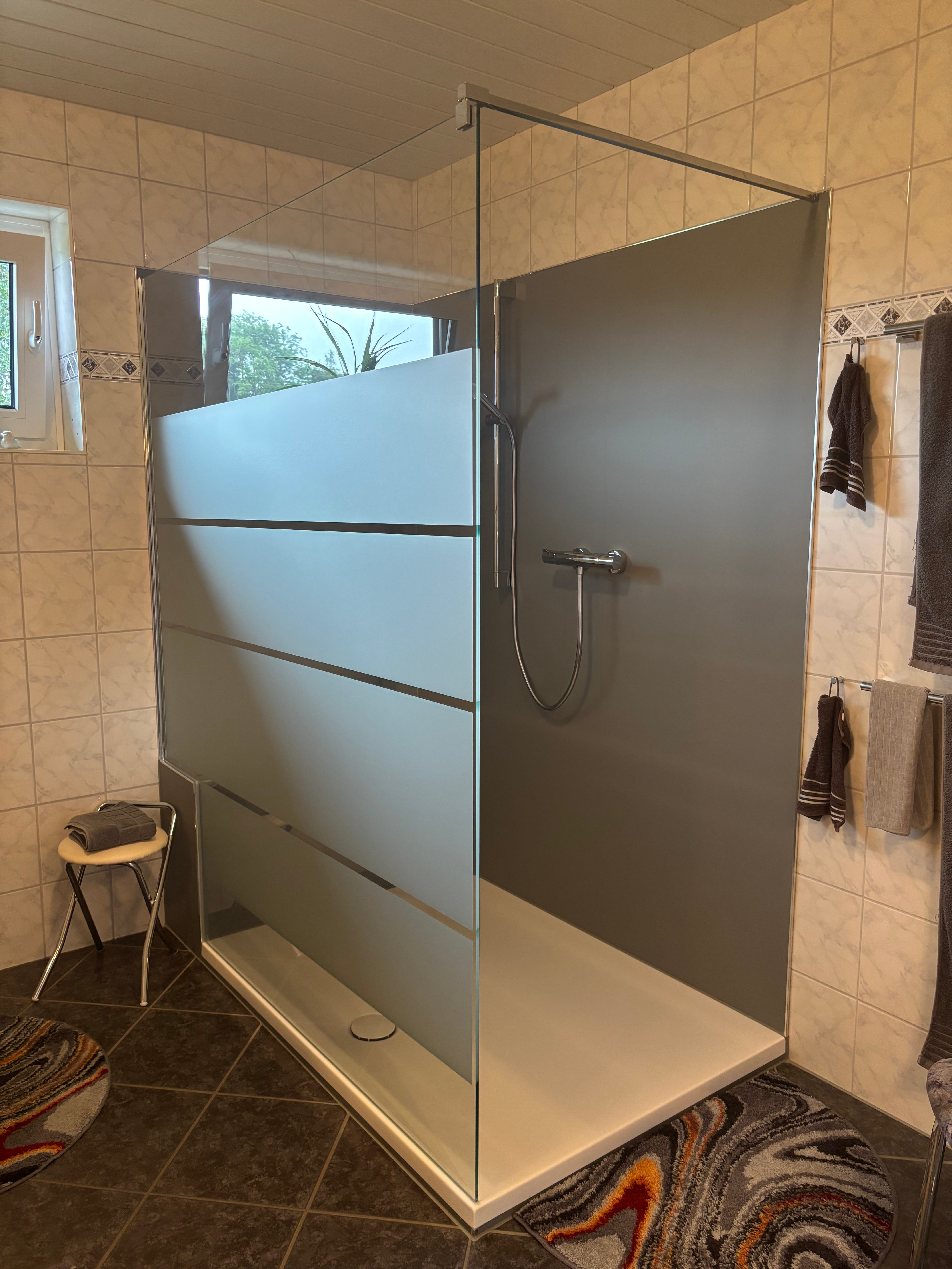 Minimalistische begehbare Dusche mit Glaswand, weißen Wänden und Holzoptikbodenbelag.