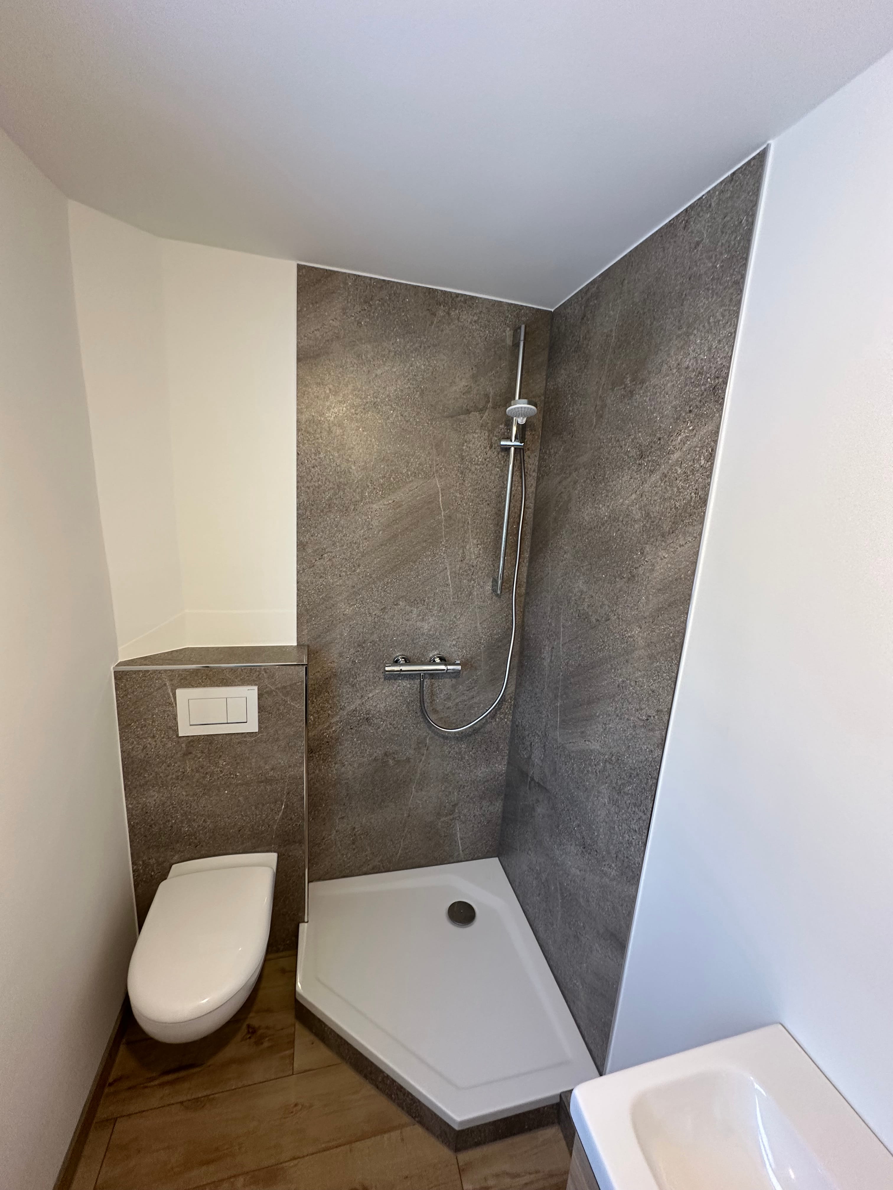 Kleines, modernes Badezimmer mit Holzfußboden, weißer Toilette, Wandwaschbecken und Schrank unter Fenster.