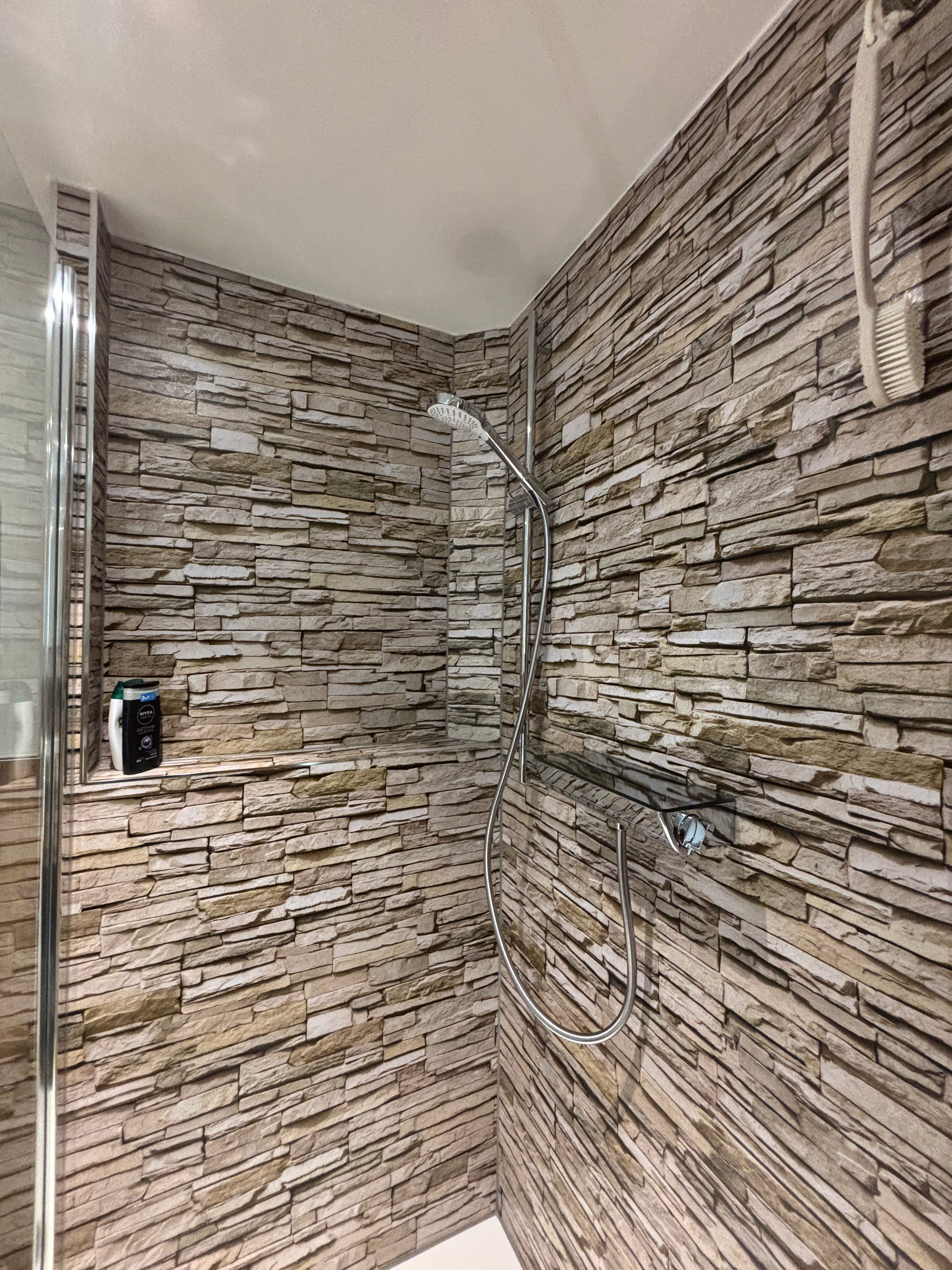 Barrierefreie Dusche mit Holzpaneelen, verchromtem Duschkopf und Sitzbank aus grauen Fliesen.