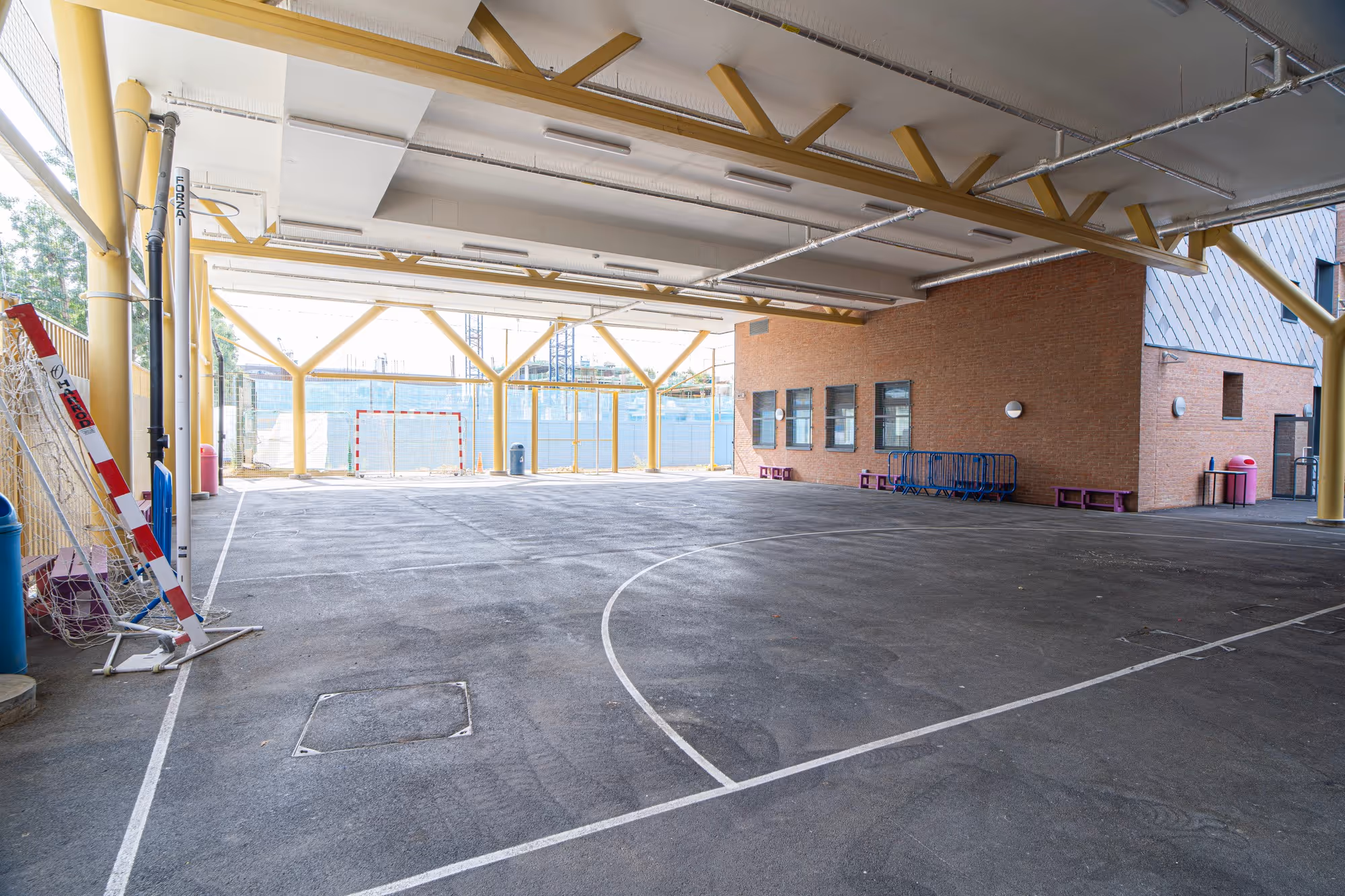 Covered outdoor sports court with handball goals, yellow beams, and brick walls under a sheltered roof.
