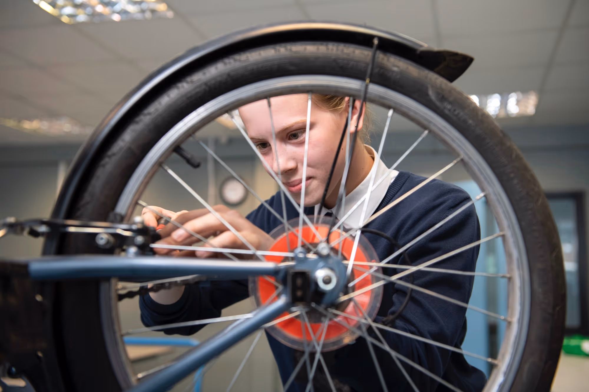 Young woman focused on repairing a bicycle wheel indoors.