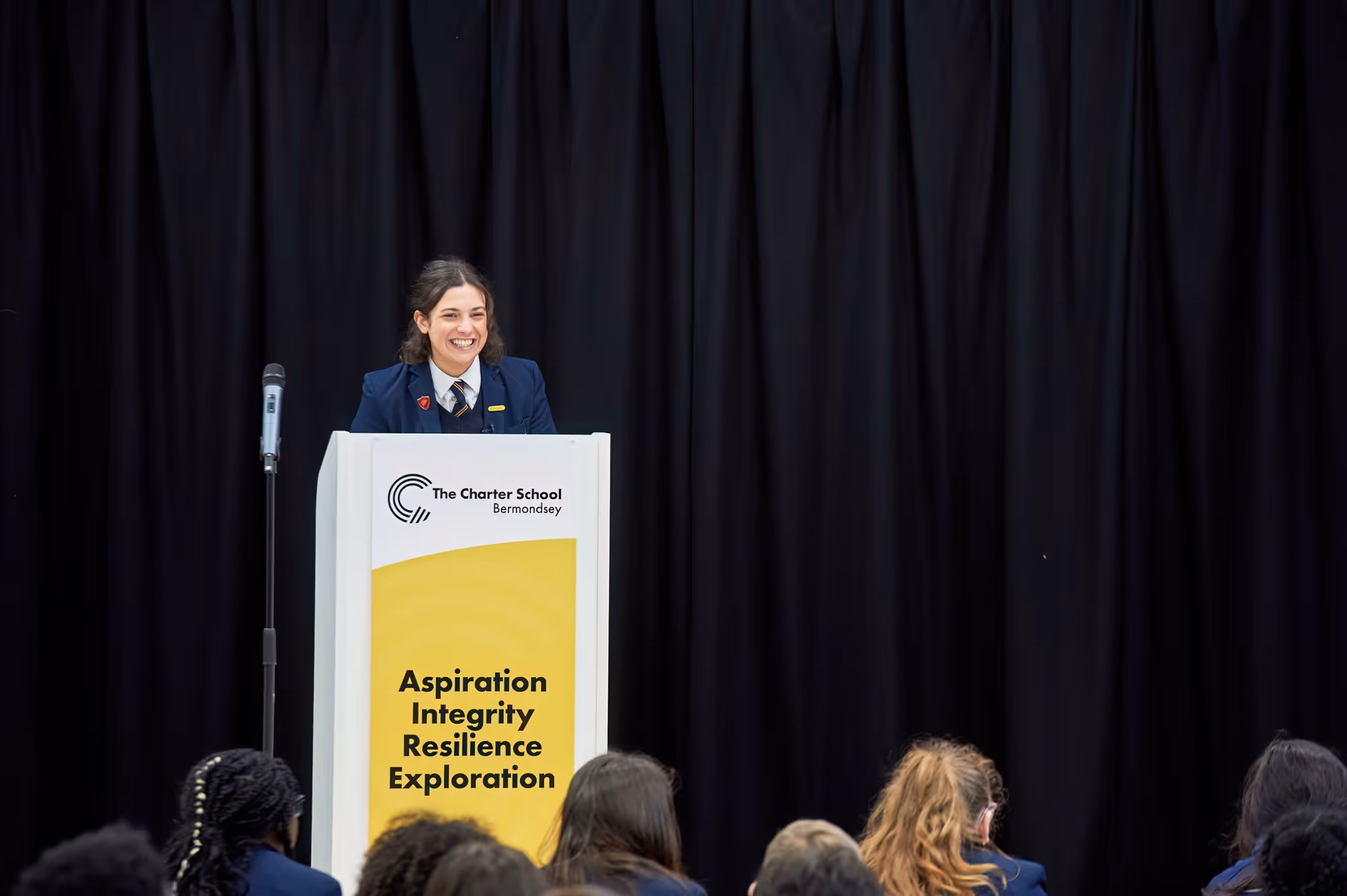 Female student smiling while speaking at a Charter School Bermondsey podium with values displayed.