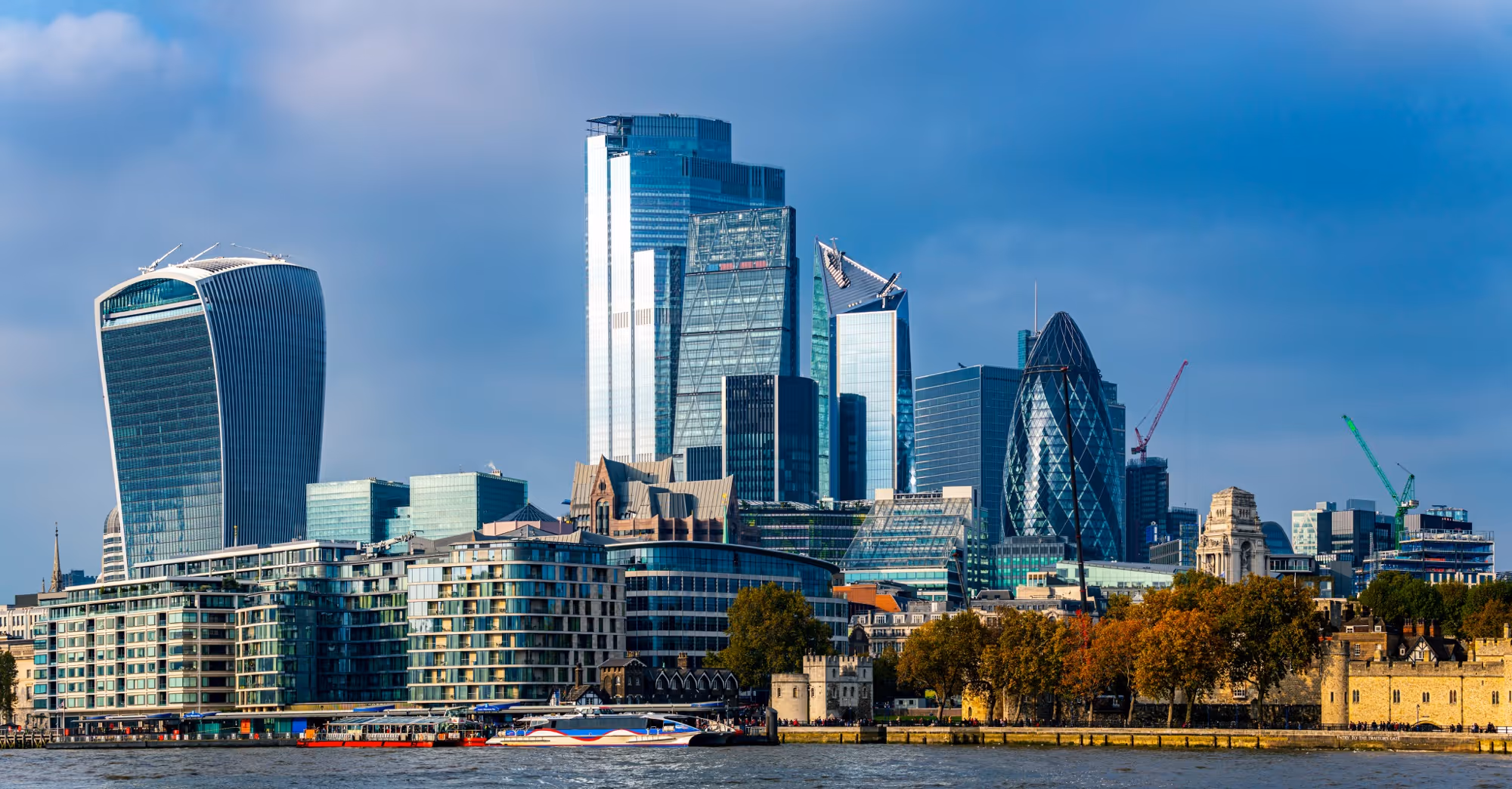 London skyline with modern skyscrapers and historic buildings along the River Thames under blue sky.