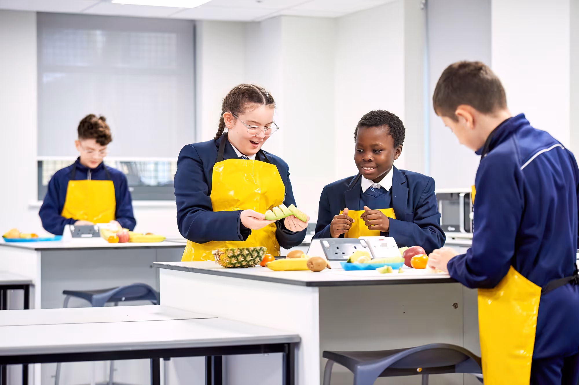 Four school children in yellow aprons preparing fruit together in a classroom kitchen.
