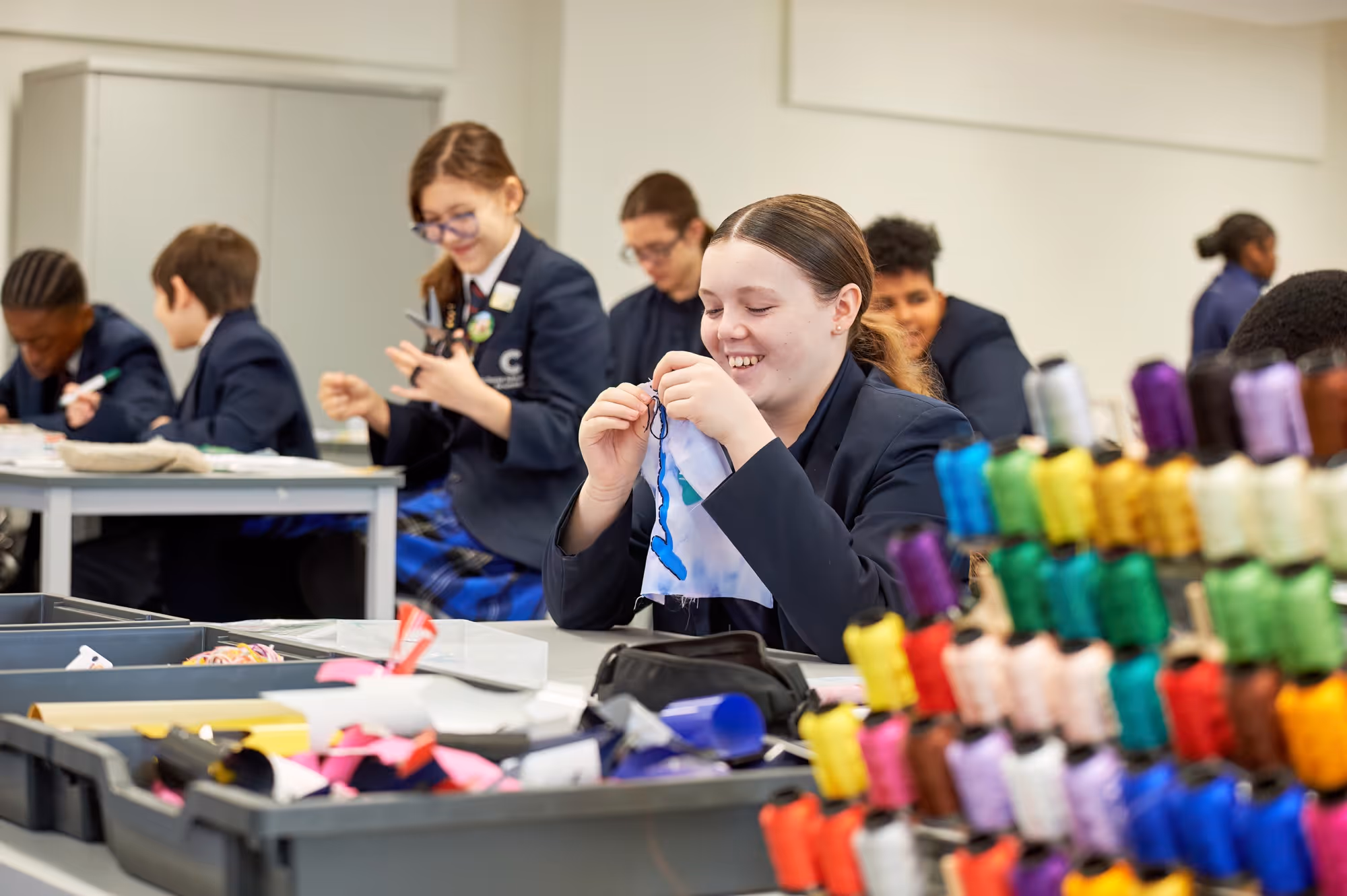 Students in school uniforms engaged in sewing and crafts in a classroom.