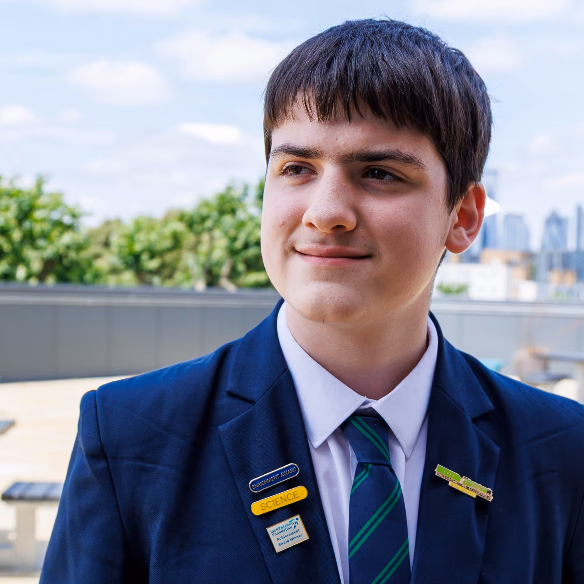 Young man in navy suit and striped tie wearing science and achievement award pins outdoors.