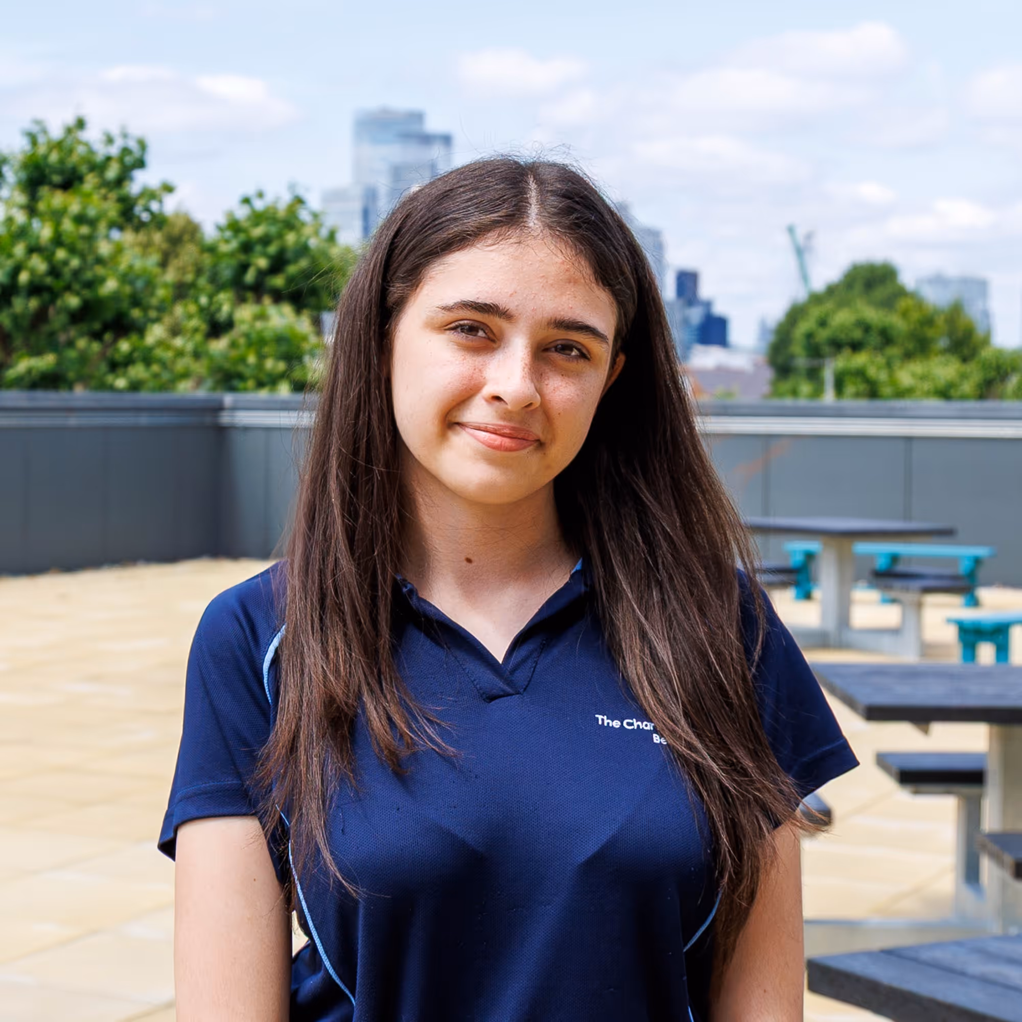 Young woman with long brown hair wearing a navy blue polo shirt outdoors in daytime.
