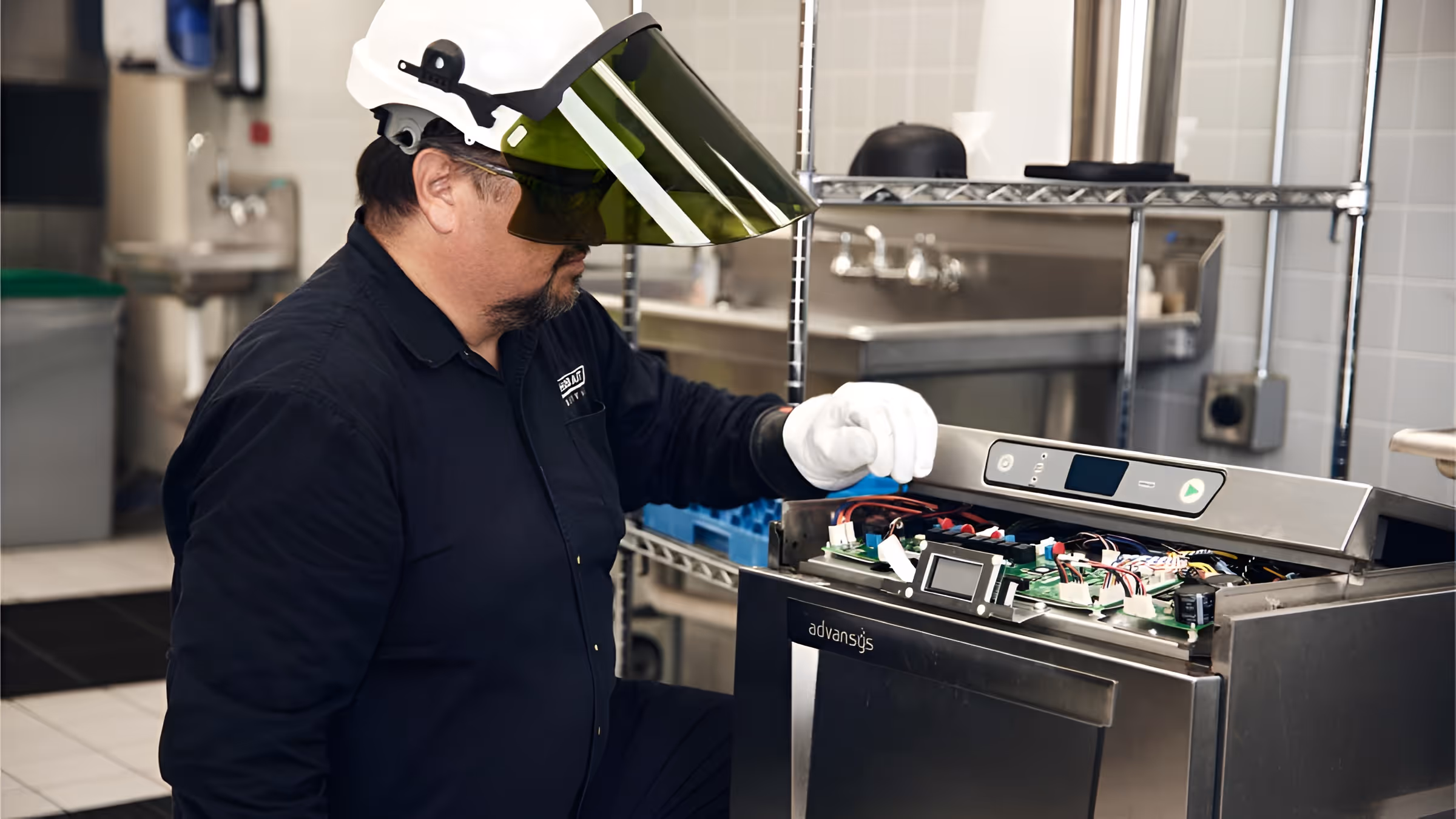 Technician wearing protective visor and gloves repairing the control panel of a commercial dishwasher.