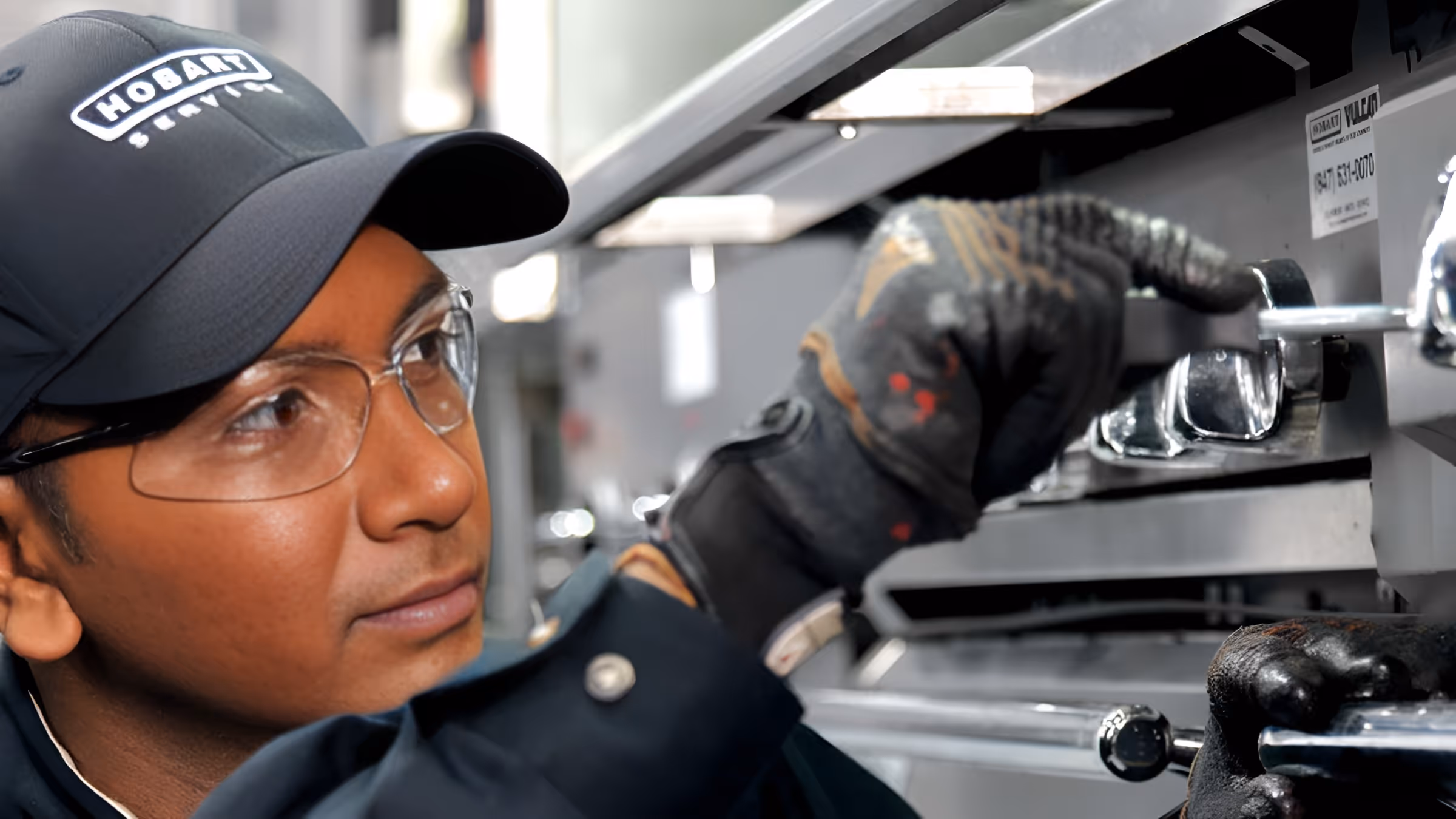 Technician wearing safety glasses and gloves adjusting control knobs on industrial equipment.