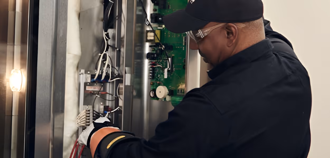 Technician wearing safety glasses and gloves working on electrical wiring inside a control panel.