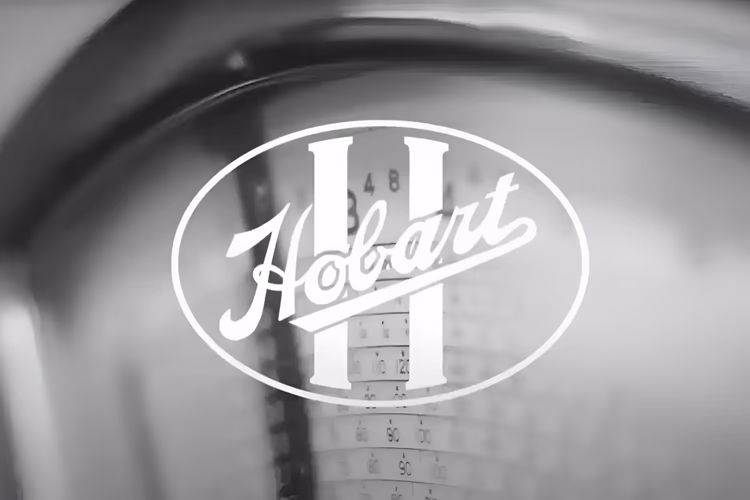 Black and white close-up of a Holbart II logo overlaid on a measuring scale background.