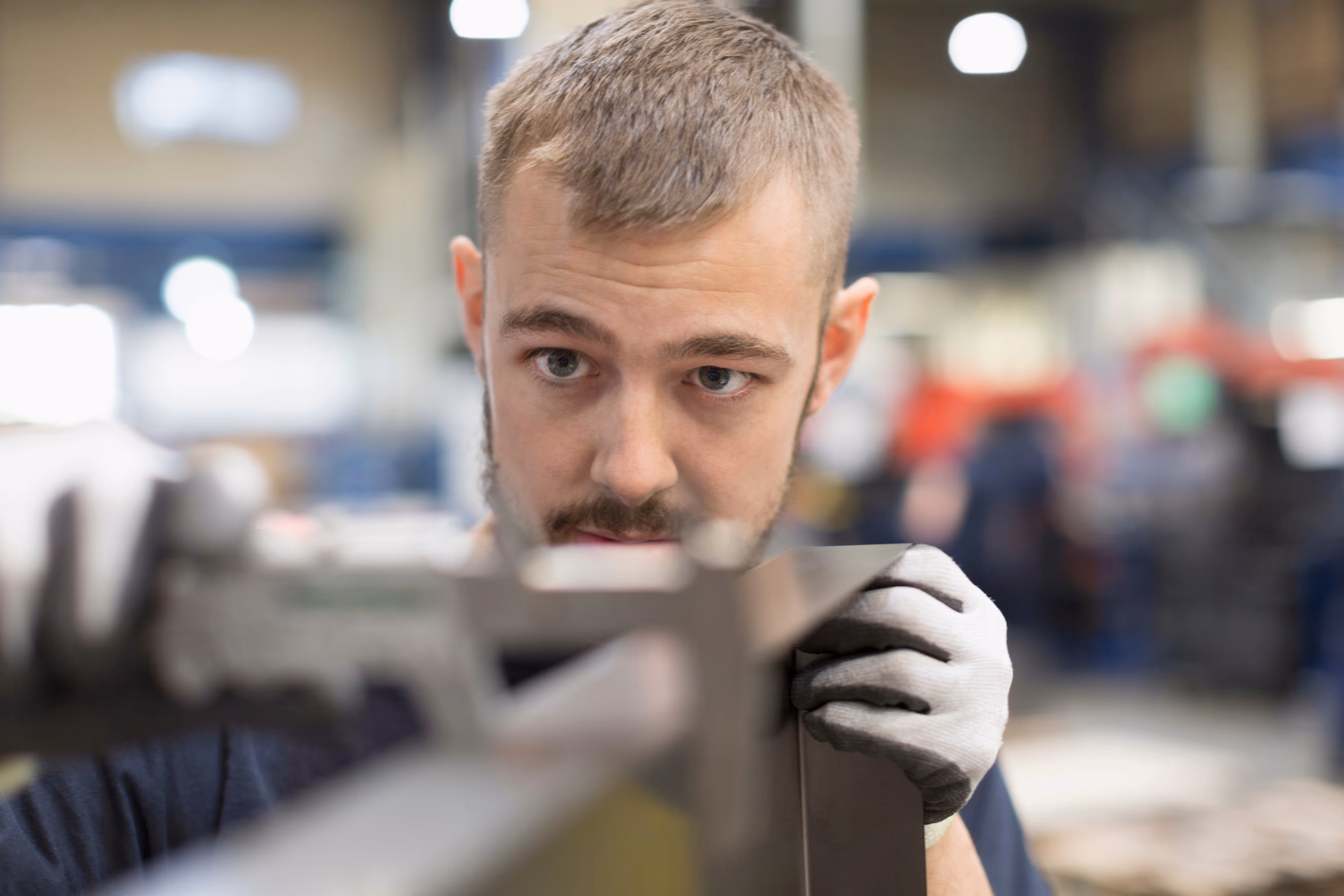 Man wearing gloves closely inspecting a metal object in a workshop.