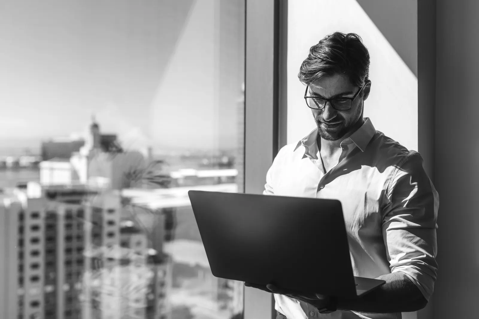 Founder working on a laptop beside an office window overlooking a city
