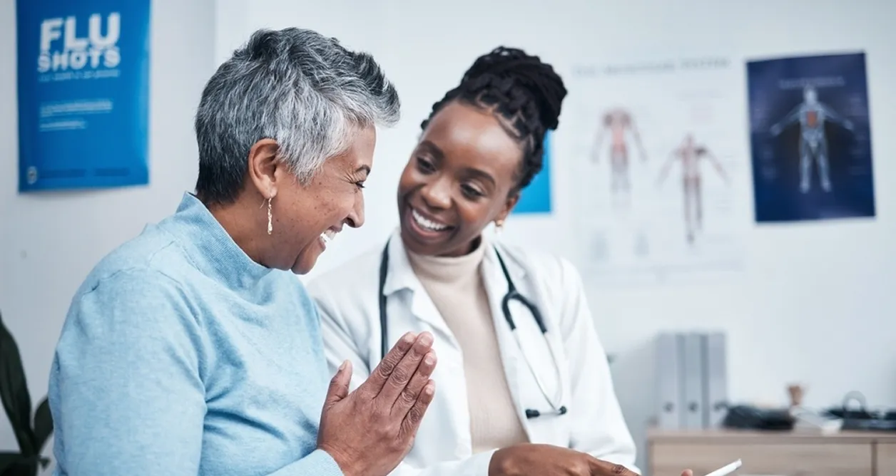 Smiling female doctor talking with happy senior woman in a medical office with a flu shots poster in the background.