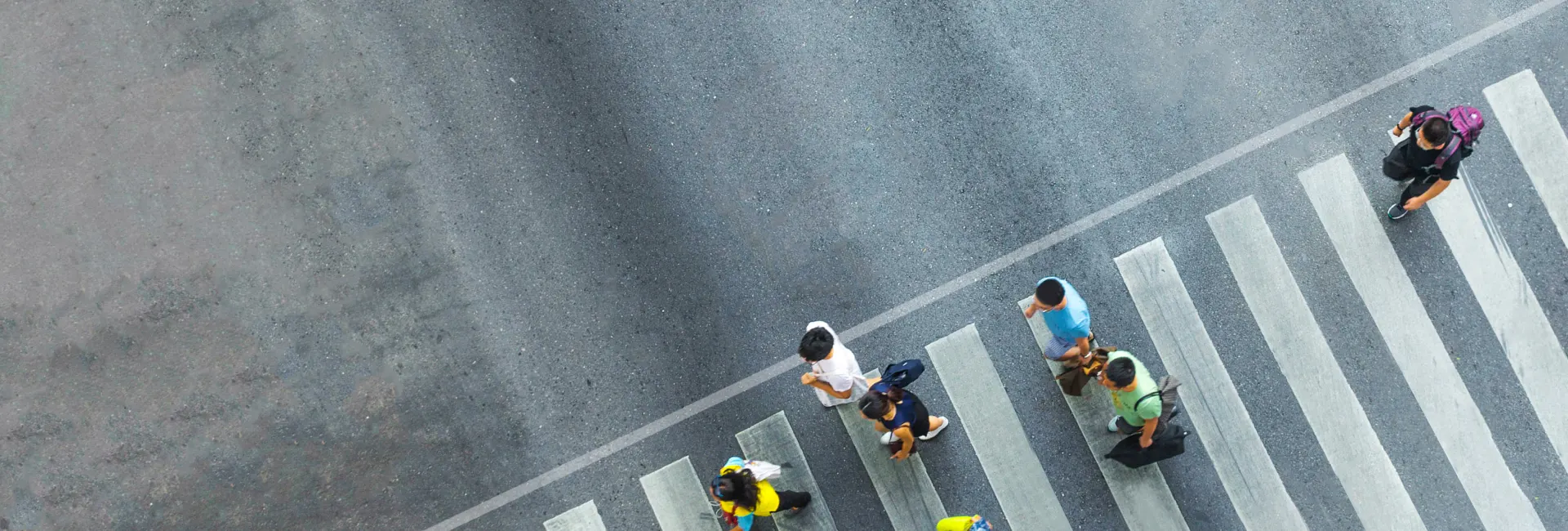 Aerial view of pedestrians crossing a large city intersection on a marked crosswalk.