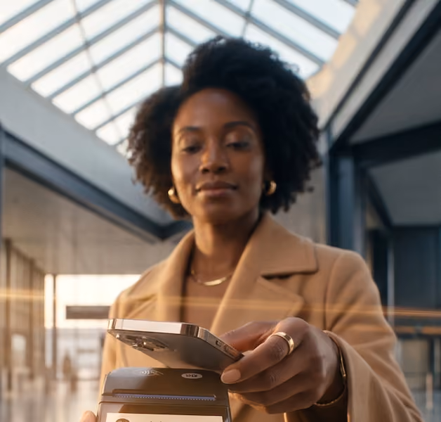 A female traveller using smartphone for contactless payment on a card reader in an airport.