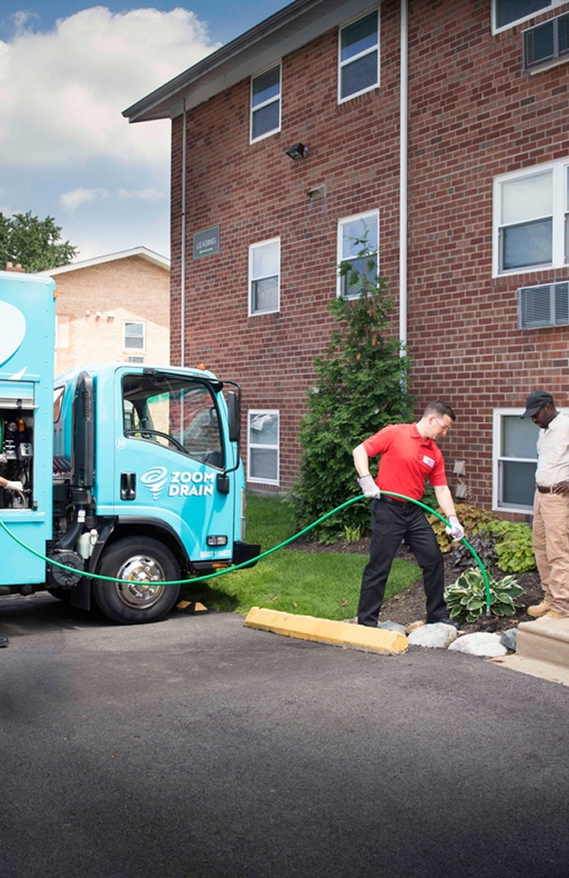 Zoom Drain truck parked outside a residential building with technician nearby.