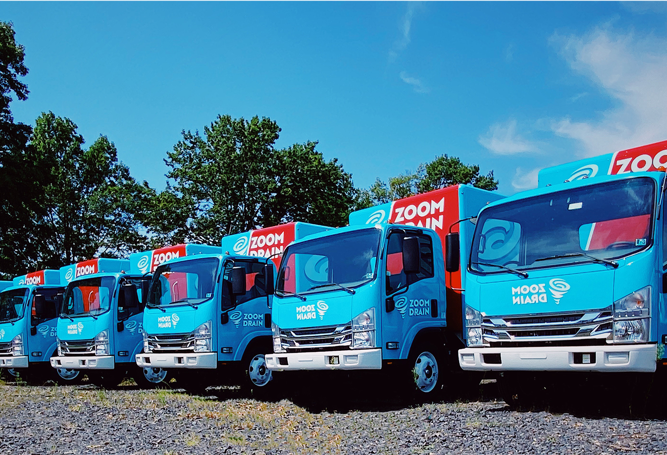 Row of Zoom Drain service trucks parked outdoors in a lot.