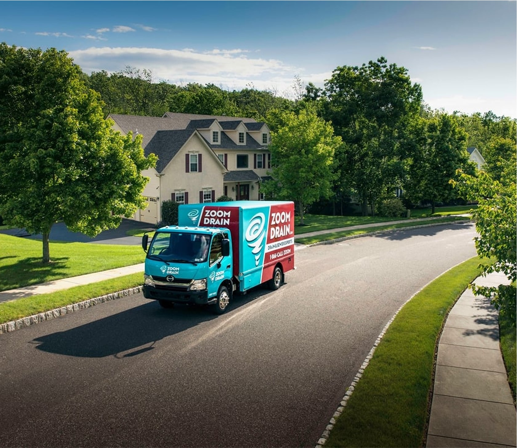Zoom Drain truck driving on a suburban street with houses in the background.