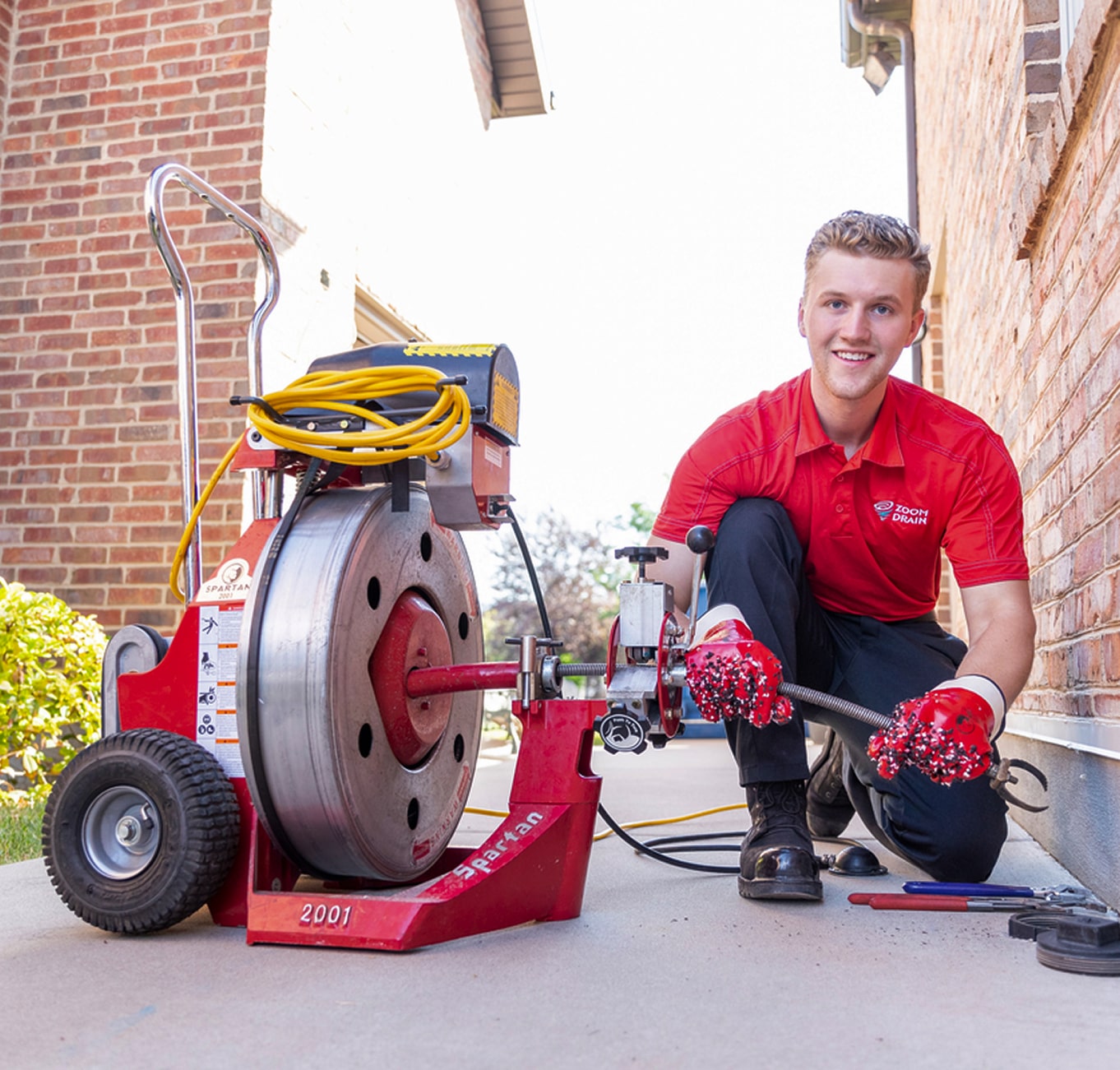 Technician operating drain cleaning equipment in a brick-walled alley.