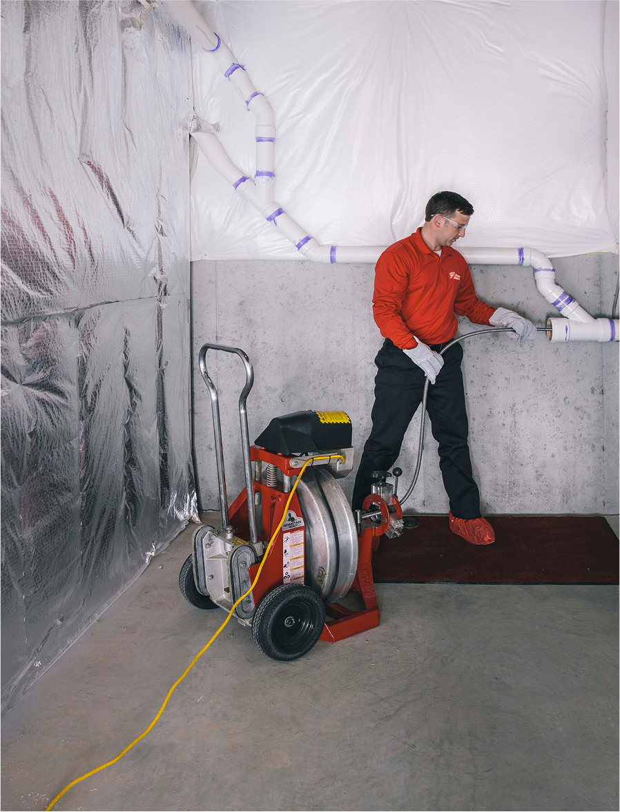 Technician operating commercial drain cleaning equipment inside a building.