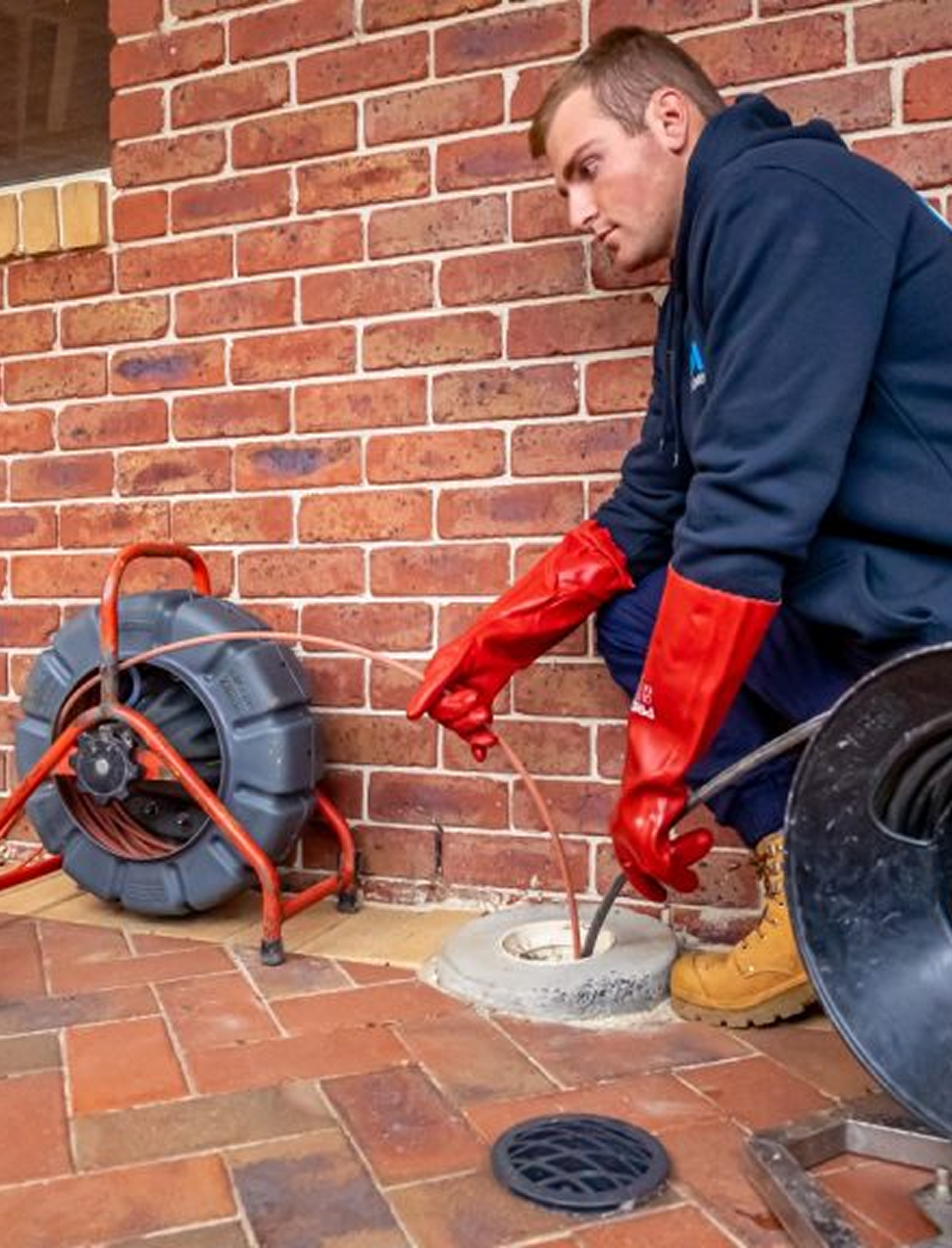 Technician cleaning a commercial drain with red hose and gloves.